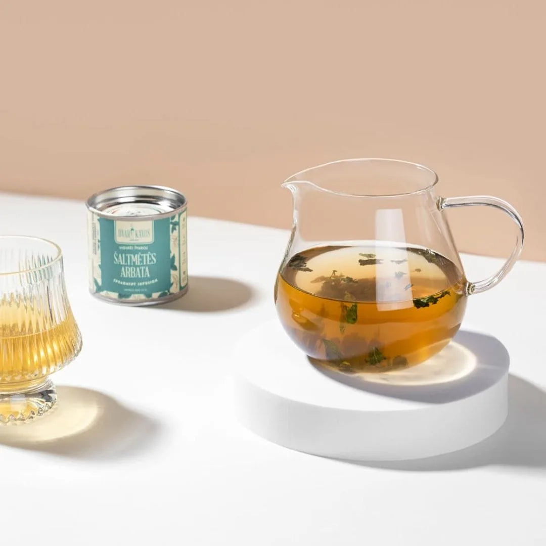 Tea-making setup with a glass teapot, glass mug, and canister on a white surface.