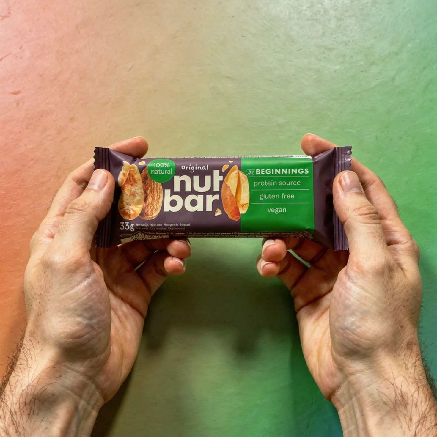 Two hands holding a NutBar protein bar against a gradient background