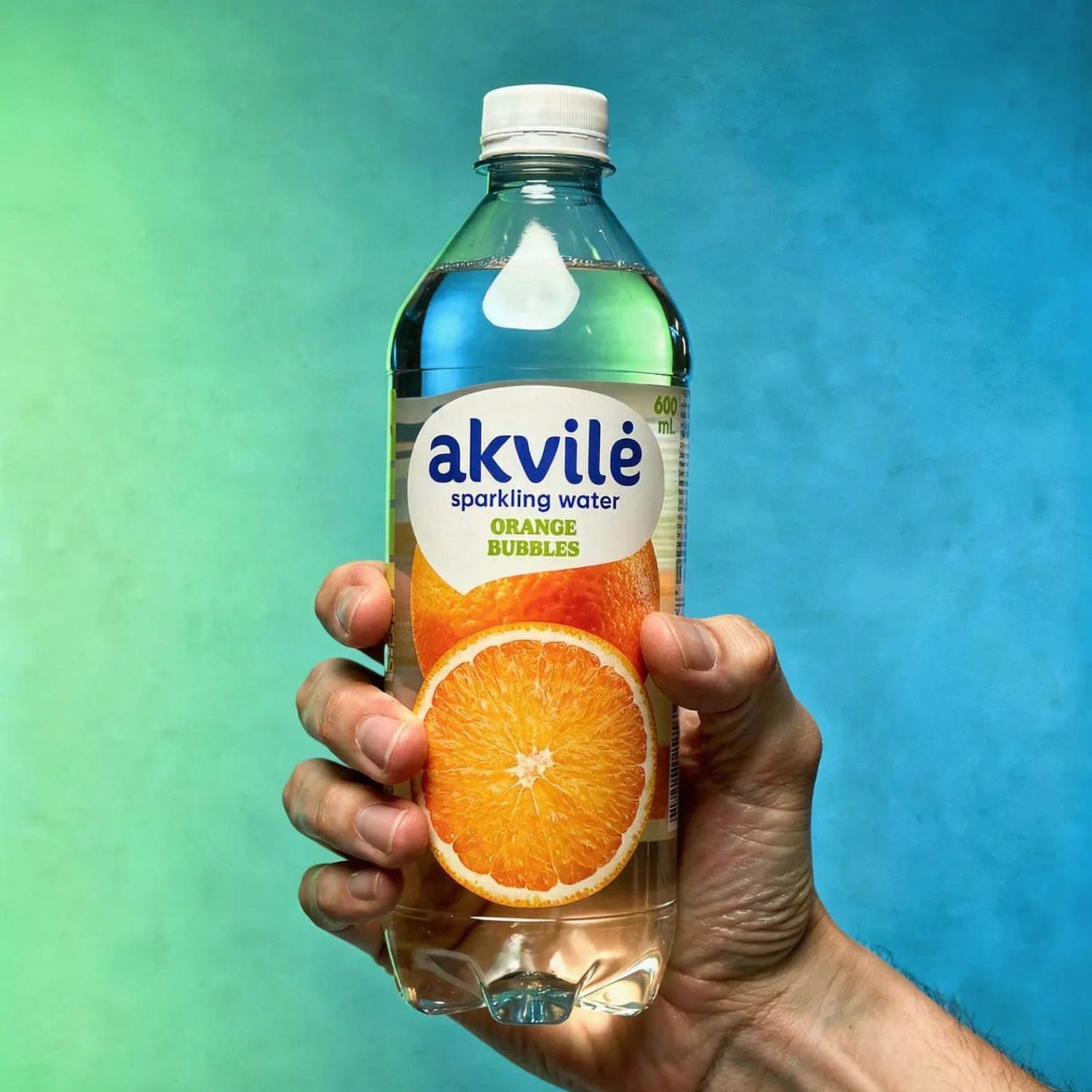 Hand holding an Akvile sparkling water bottle with an orange slice against a gradient background