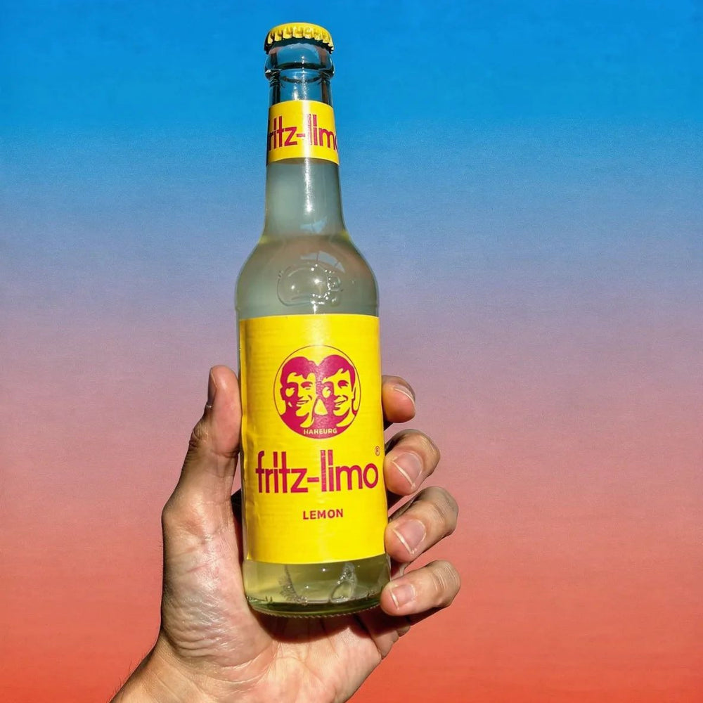 Hand holding a bottle of fritz-limo against a colorful gradient background
